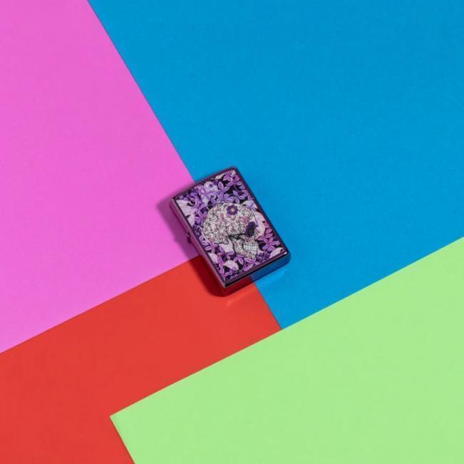 Lifestyle image of Hidden Skull Design high polish purple Windproof Lighter laying flat on neon coloured background