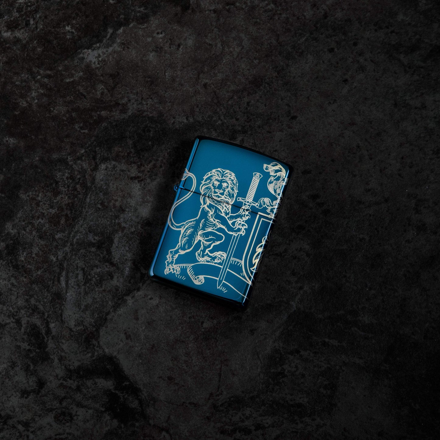 Lifestyle image of Medieval Coat of Arms 360° Design High Polish Blue Windproof Lighter laying on a dark background