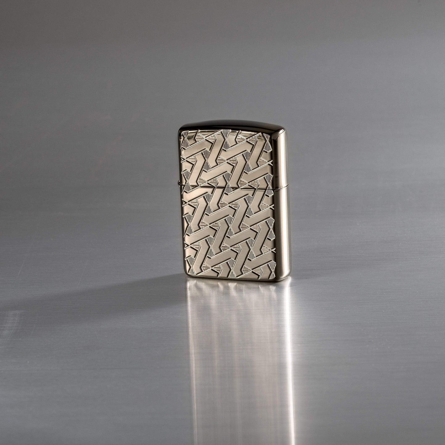 Lifestyle image of Armor Geometric Weave High Polish Black Ice Windproof Lighter standing on a reflective surface