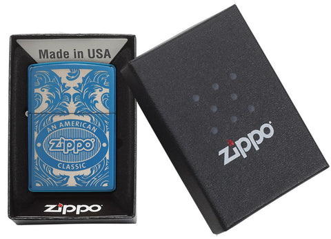 Blaues Zippo-Feuerzeug von vorne gesehen in einer offenen schwarzen Geschenkbox, umgeben von einem lasergravierten, filigranen Motiv mit dem Zippo-Logo und 